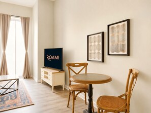 Ein Zimmer mit Fernseher, zwei gerahmten Bildern, einem Esstisch mit Stühlen, einem Holzschrank und einem gemusterten Teppich.