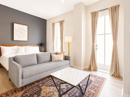 A modern hotel room with a grey sofa, a white coffee table, and a patterned rug.