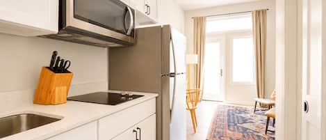 Una cocina moderna con microondas, estufa y refrigerador. En la encimera, hay un organizador de utensilios de madera.