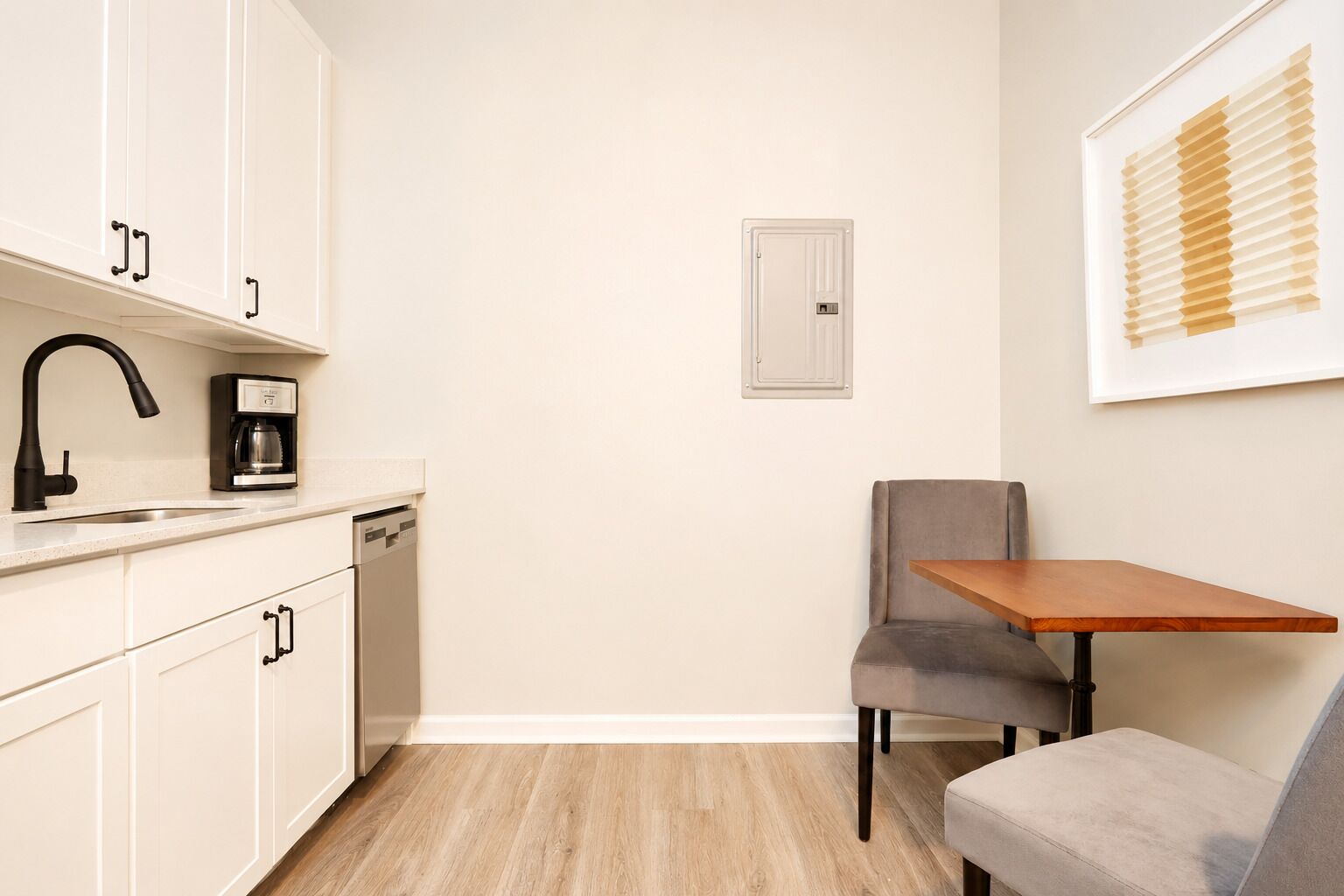 A compact kitchen with a coffee maker, dishwasher, and a small table with a chair.