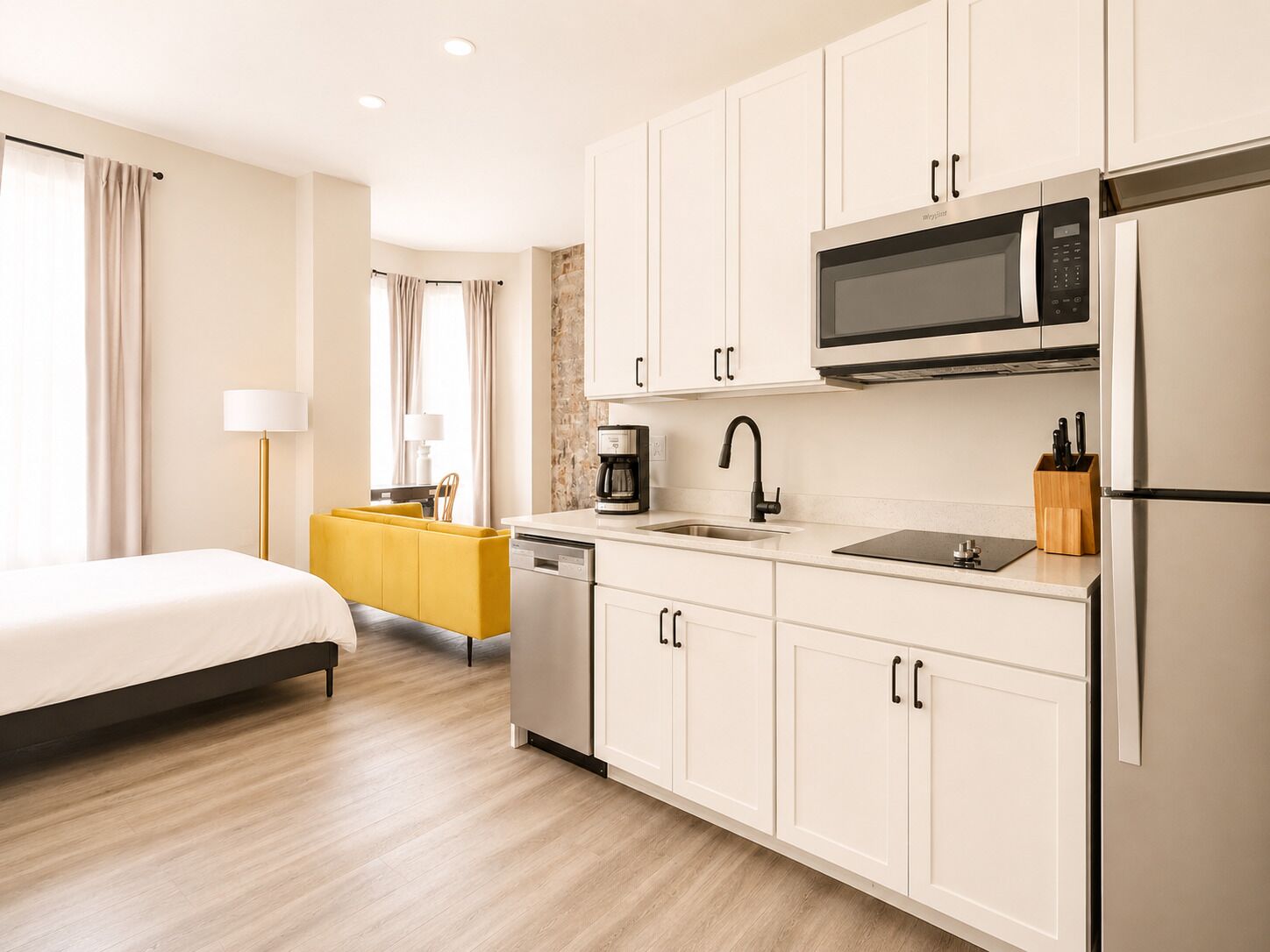 Une chambre d’hôtel moderne avec un lit, un canapé jaune et un coin cuisine équipé d’un four à micro-ondes, d’un évier et d’un réfrigérateur.