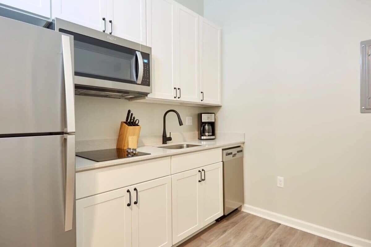 A modern kitchen with white cabinets, a stainless steel refrigerator, a microwave, a coffee maker, and a dishwasher.
