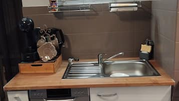 A compact kitchen with a sink, a coffee machine, and a dish rack.