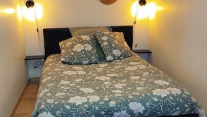 Un lit recouvert d’une couvre-lit à motifs floraux, deux lampes fixées au mur, une tapisserie murale tissée et un tapis tissé sur le sol.