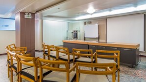 Un salón de conferencias con sillas de madera, una mesa grande, una pizarra y una kitchenette.
