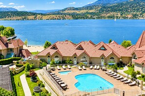 A resort with a swimming pool, lounge chairs, and a view of a lake and mountains.