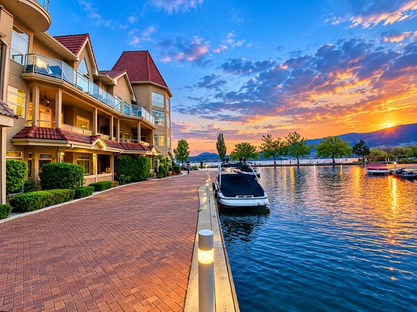 A waterfront hotel with a paved walkway, a boat dock, and a sunset view.