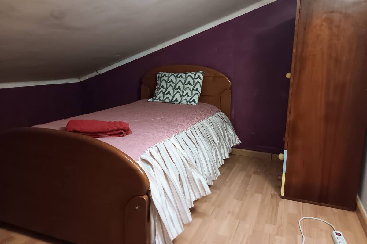 A bedroom with a wooden bed, purple walls, a wooden wardrobe, and a wooden floor.