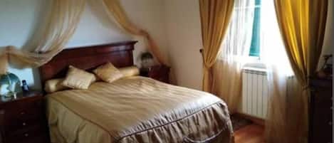 A bedroom with a large bed, a nightstand, a dresser, and a window with curtains.
