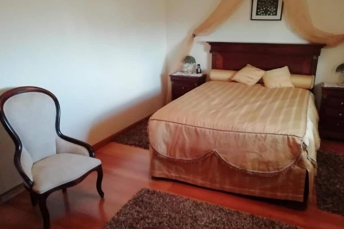 A bedroom with a bed, a chair, a nightstand, and a decorative canopy.