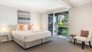 A modern bedroom with a large bed, a chair, a nightstand, and a view of the outdoors.