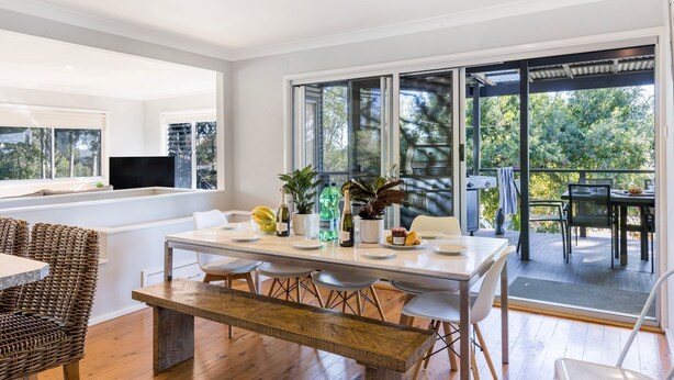 A modern dining area with a wooden bench, white chairs, and a table set for two.