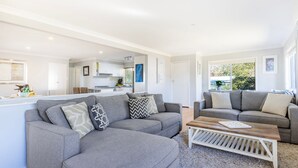 A modern living room with two grey sofas, a wooden coffee table, and a kitchen in the background.