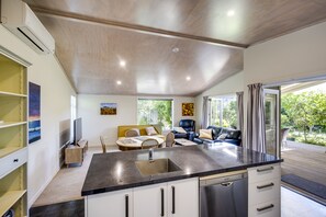 A modern kitchen with a central island, a dining area with a table and chairs, and a living area with a sofa and a TV. - Garden Retreat - Napier Holiday Home (Napier)