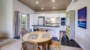 Une cuisine moderne avec des meubles blancs, un îlot central et un coin repas comprenant une table ronde et des chaises en osier.