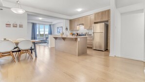 A modern kitchen with wooden cabinets, a stainless steel refrigerator, and a dining area with a table and chairs.