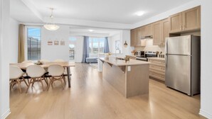 A modern kitchen with wooden cabinets, a stainless steel refrigerator, and a dining area with a table and chairs.