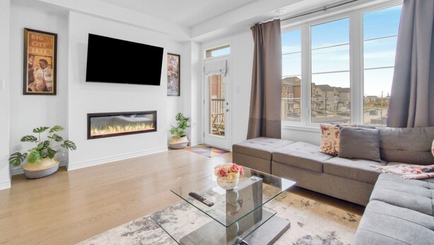 A modern living room with a grey sofa, a flat-screen TV mounted on the wall, and a fireplace.
