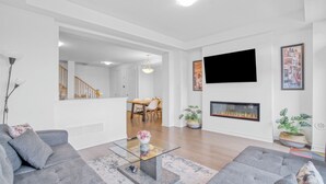 A modern living room with a fireplace, grey sofas, a glass coffee table, and a flat-screen TV mounted on the wall.