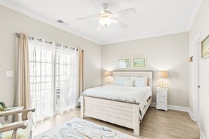Un dormitorio con cama, mesitas de noche, ventilador de techo y vistas a través de una ventana con cortinas.