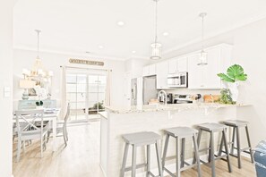 A modern kitchen with white cabinets, a central island with stools, and a dining area with a white table and chairs.
