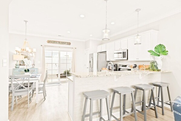 A modern kitchen with white cabinets, a central island with stools, and a dining area with a white table and chairs.