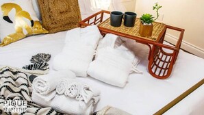 A neatly made bed with white linens, a woven tray with two black mugs and a small plant, and a zebra-patterned blanket. - Tropical Oasis - King Beds - Garage - Long Stays! (Edmonton)