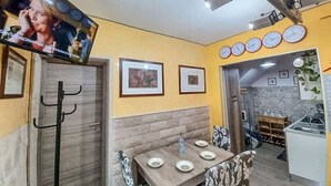 Zona de menjador amb una taula preparada per a quatre, un televisor fixat a la paret i una cuina visible al fons.