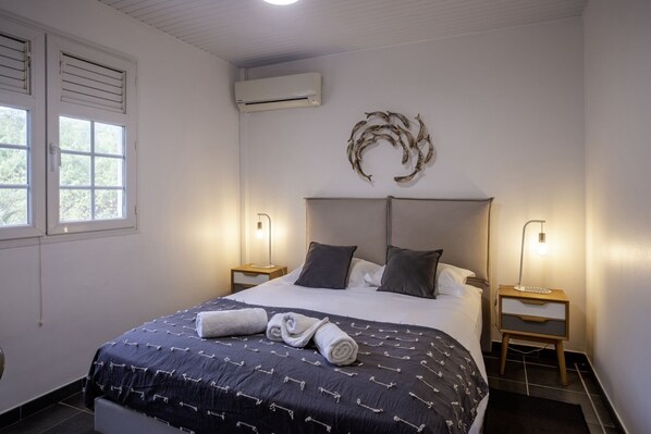 A bedroom with a large bed, two bedside tables with lamps, an air conditioning unit, and a decorative wall piece.