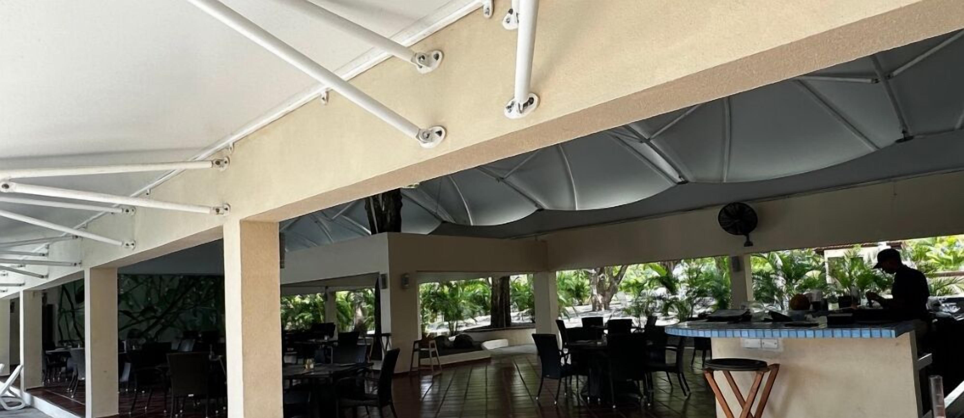 An outdoor dining area with tables and chairs, a bar, and a view of greenery.