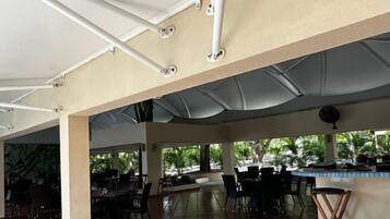 An outdoor dining area with tables and chairs, a bar, and a view of greenery.