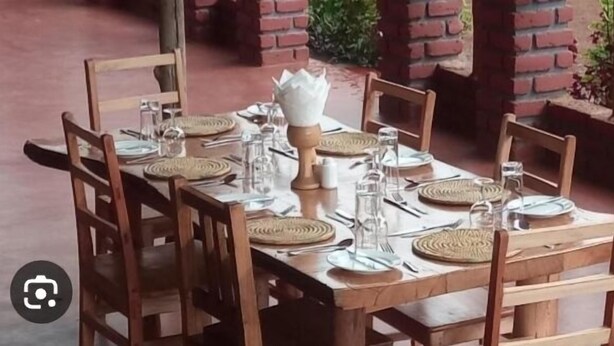 A wooden dining table set with plates, cutlery, and glassware, surrounded by chairs. - Heaven GetAway lodge  (Arusha)