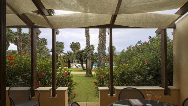 A covered outdoor seating area with a view of a pool and palm trees. - Tranquil Lantana Resort 2 Bedroom Apartments Sleeps 7 Persons (Pula)