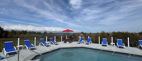 Un área de piscina con sillas reclinables azules y una sombrilla roja.
