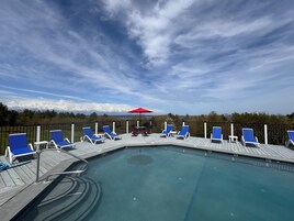 Un área de piscina con sillas reclinables azules y una sombrilla roja.