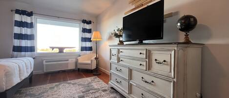 A bedroom with a bed, a dresser, a television, and a window with curtains.