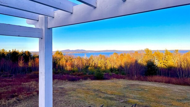 A white pergola structure with a clear view of a lake and mountains in the distance. - Acadia Ocean View Hotel (Bar Harbor)