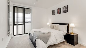 A modern bedroom with a large bed, a nightstand with a lamp, and a view through a sliding door. - The Water - Aqua Apt (London)