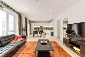 A modern living room with a black leather sofa, a coffee table, and a flat-screen TV. - The Crow - 1 Bedroom Apt (London)
