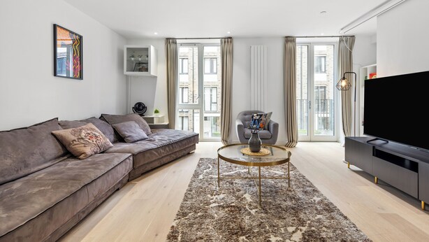 Een moderne woonkamer met een bank, fauteuil, televisie en een groot raam met gordijnen.