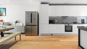 Een moderne keuken met witte kastjes, een roestvrijstalen koelkast, een inbouwoven en een houten vloer.