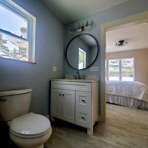 A bathroom with a toilet, a sink, and a mirror. There is a window providing natural light and a view of trees outside. - Lakefront Cottage with sauna and private dock. (Washington)