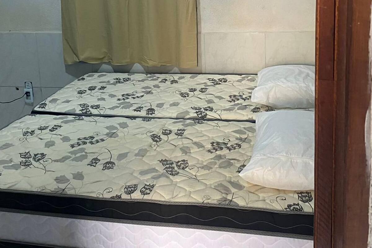 A small, single-bed room with a floral-patterned mattress, a wooden headboard, and a curtain.