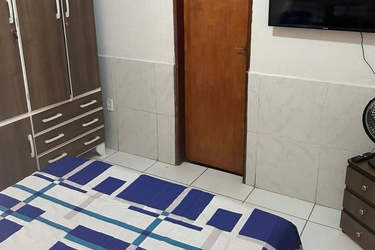 A bedroom with a bed, a wardrobe, a television, and a fan.