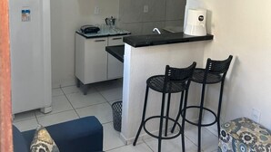 Ett kompakt bostadsutrymme med ett litet kök, en soffa, två stolar och en mönstrad pall.