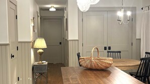 A dining area with a wooden table, chairs, a chandelier, and a lamp. - Quaint Village Cottage (Hartwick)
