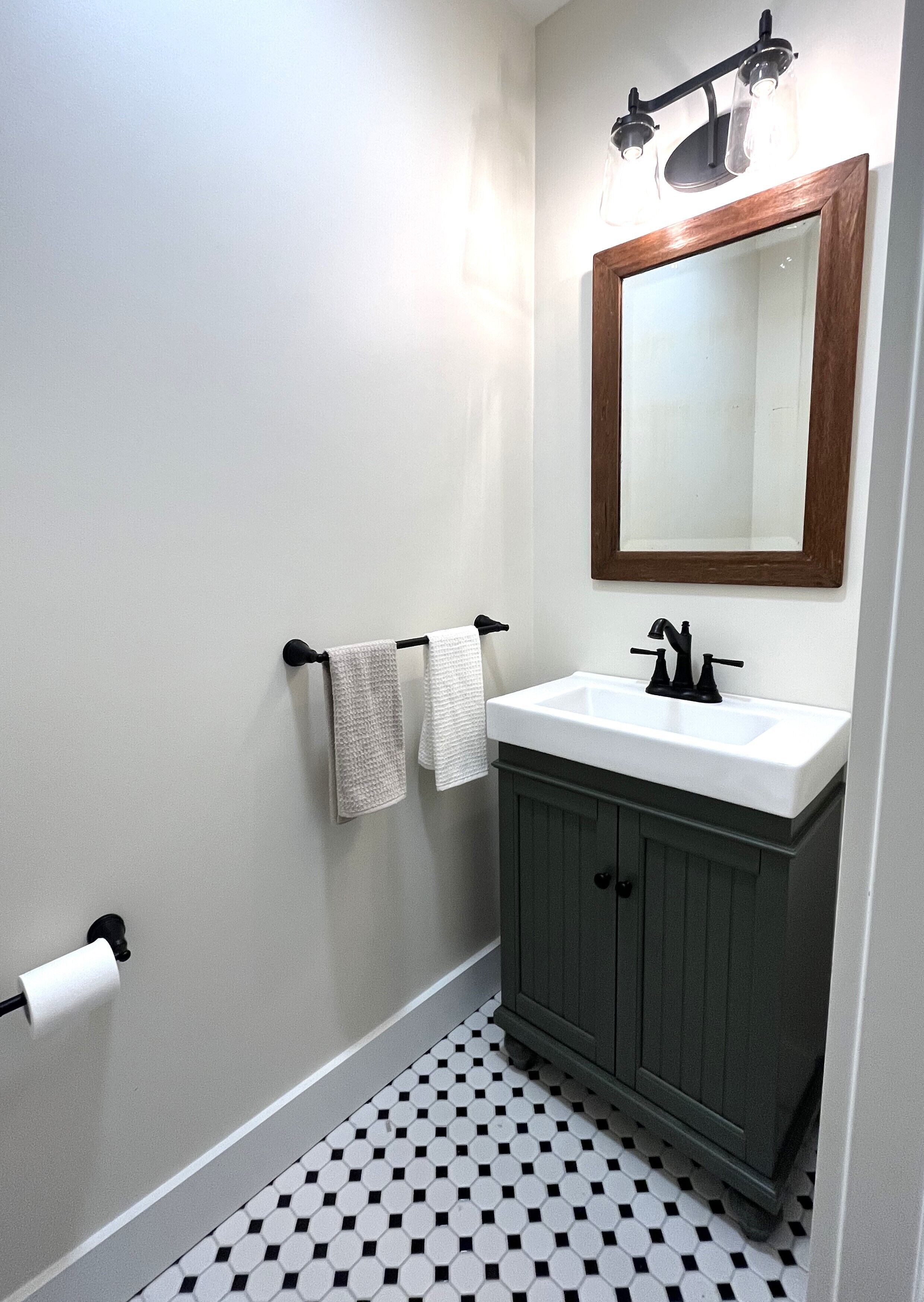 A bathroom with a white sink, dark cabinet, and a mirror with a wooden frame.