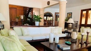 A spacious living room with a white sofa, a coffee table with books and decorative items, and a staircase in the background. - Rancho Utairs
 (La Romana)