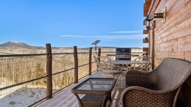 A wooden cabin with a balcony, furnished with wicker chairs and a table, overlooking a mountainous landscape. - Spacious Mountain Chalet (Park County)