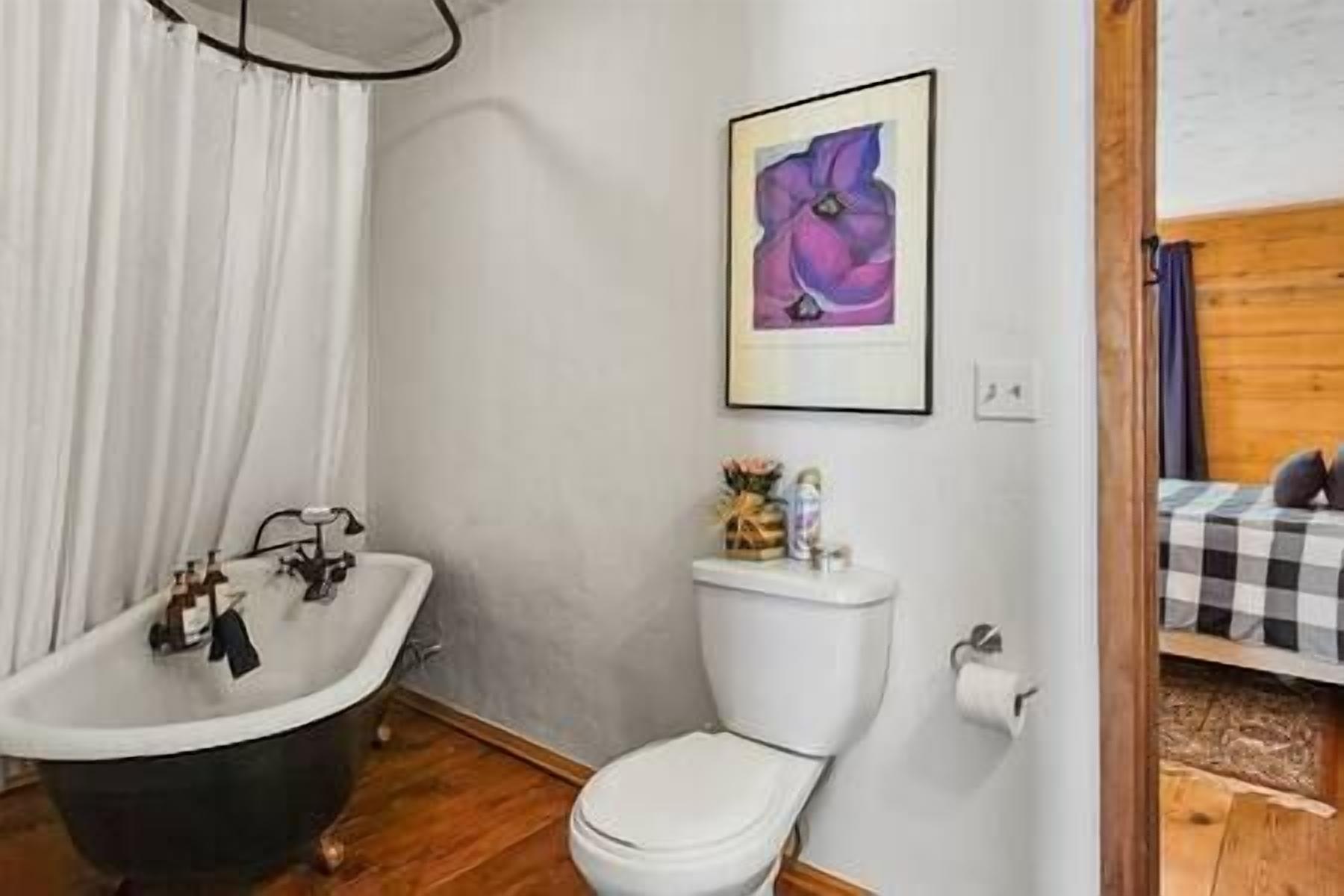 A bathroom with a white bathtub, a white toilet, and a framed artwork on the wall.